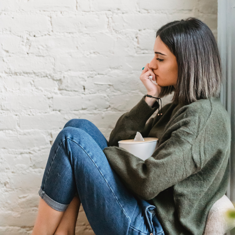 zmęczona, zamyślona kobieta siedzi z pociągniętymi kolanami, ręką podtrzymuje brodę