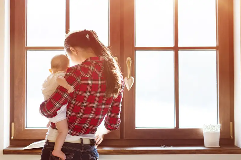 mama z dzieckiem na rękach, stojąca przy oknie