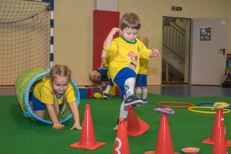 Dwoje małych dzieci przechodzi przez tor przeszkód na zajęciach sportowych Socatots