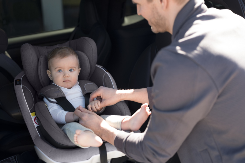 mężczyzna zapinający dziecko w foteliku samochodowym