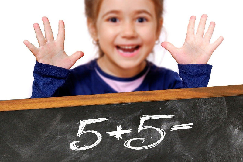 uśmiechnięta dziewczynka przy tablicy na której zpisane jest działanie matematyczne